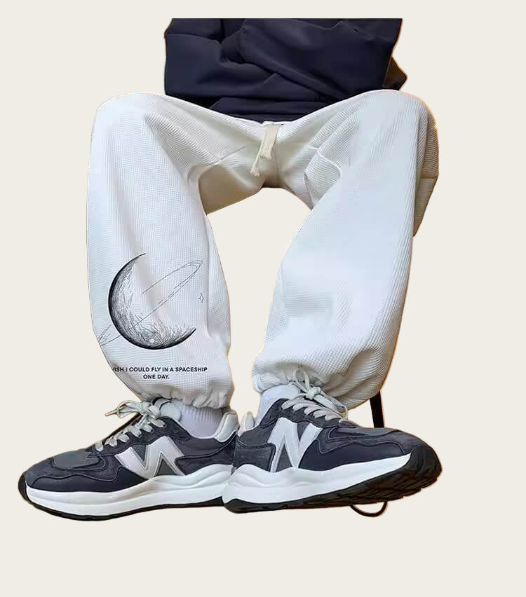 Person wearing white pants with a design and dark sneakers