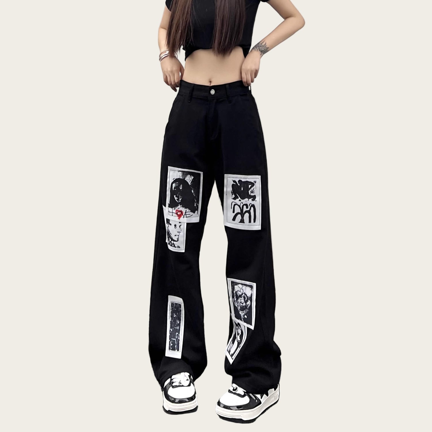 Person wearing black pants with graphic designs against a yellow wall.