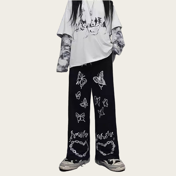 Person wearing a white oversized shirt and black pants with butterfly designs, standing.