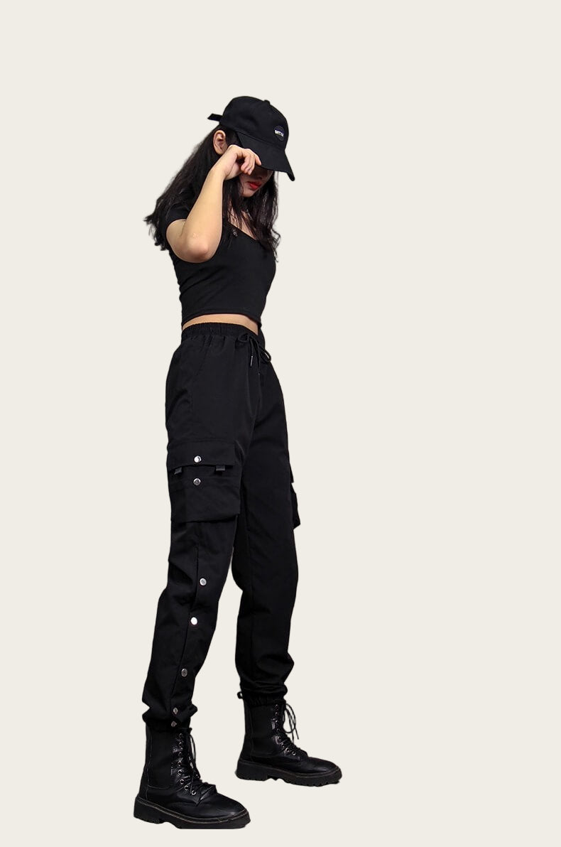 Person wearing black cargo pants and a black cap against a yellow background