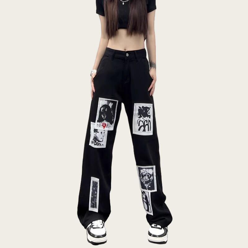 Person wearing black pants with graphic designs against a yellow wall.