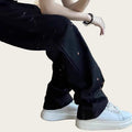 Person wearing black pants with small colorful dots and white sneakers in a room.