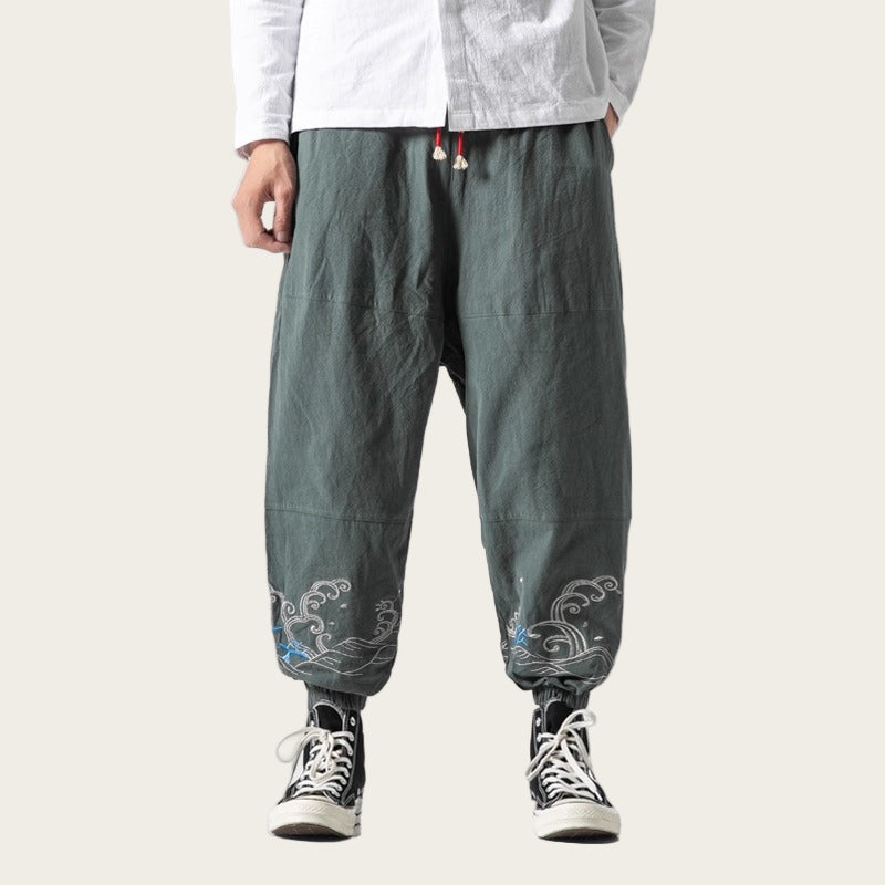 Person wearing dark green pants with floral embroidery on a yellow background