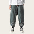 Person wearing dark green pants with floral embroidery on a yellow background