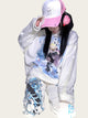 Person wearing a white hoodie with graphic design, pink cap, and white pants.