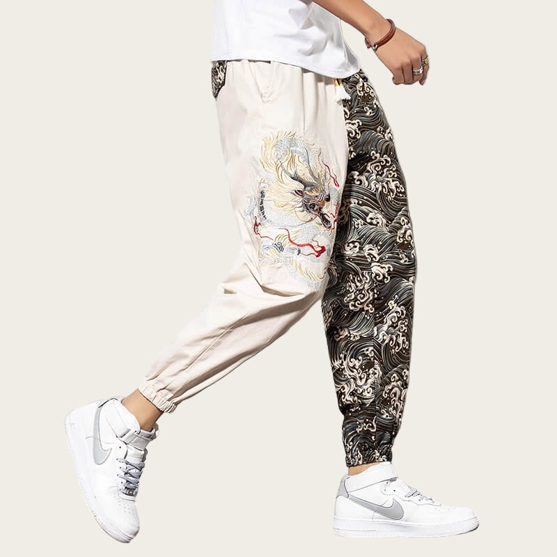 Person wearing a white top, beige pants with dragon design, and black pants with wave design, standing.