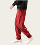 Person wearing red pants with a logo, white sneakers, and a black top in a minimalistic setting.