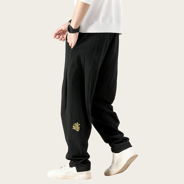 Person wearing black pants with a logo, standing in a room.