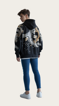 Person wearing a black hoodie with intricate designs on a plain background