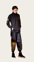 Person wearing a black outfit with gold accents against a neutral background