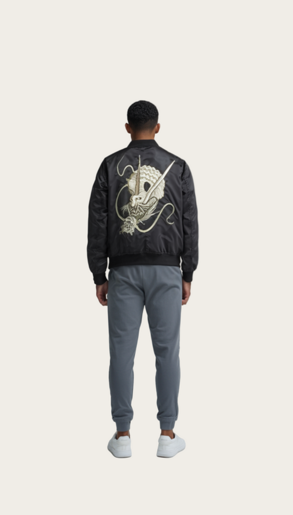 Person wearing a black bomber jacket with a gold design on the back, standing against a plain background.