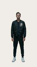 Person wearing a black bomber jacket with a logo on a gray background