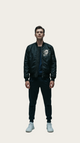 Person wearing a black bomber jacket with a logo on a gray background