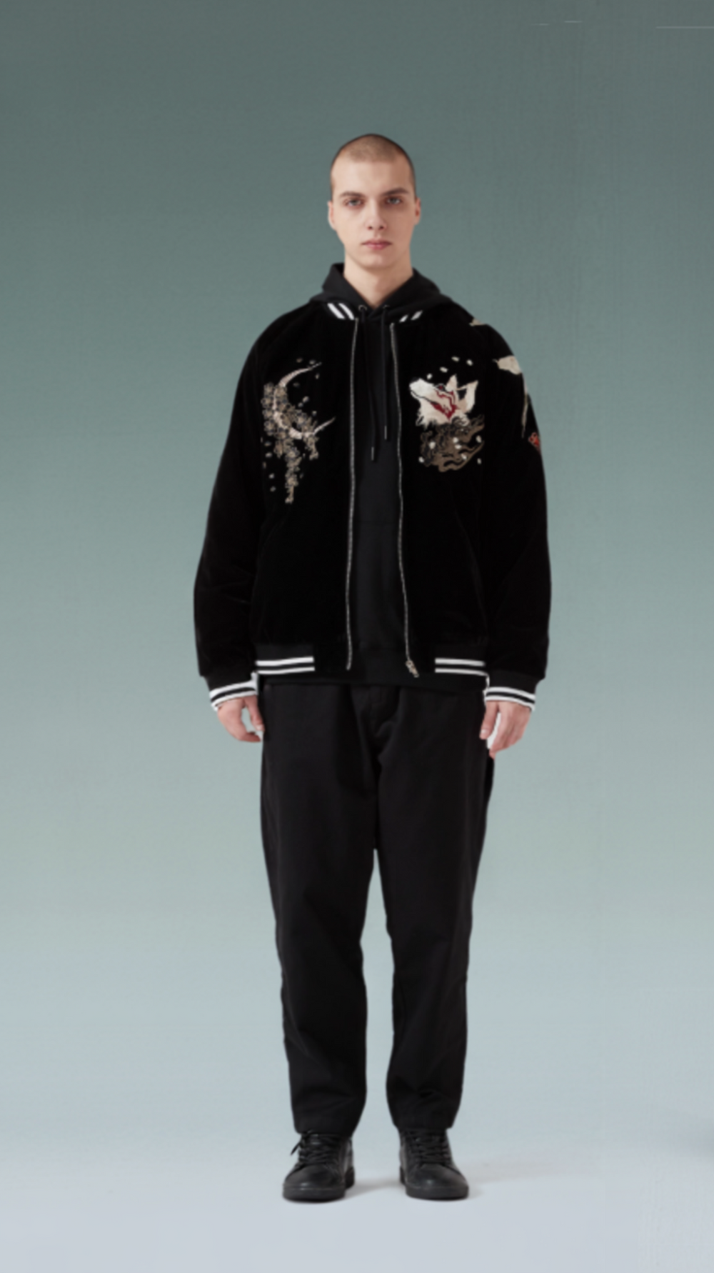 Person wearing a black jacket with embroidered designs on a gray background