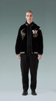 Person wearing a black jacket with embroidered designs on a gray background