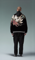 Person wearing a black jacket with floral embroidery on the back against a gray background