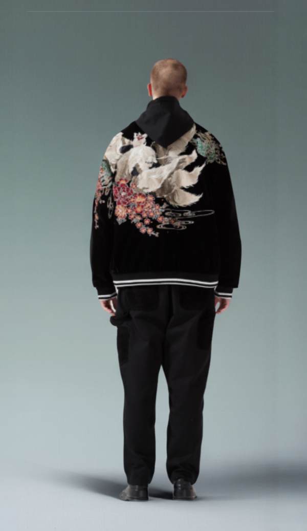 Person wearing a black jacket with floral embroidery on the back against a gray background