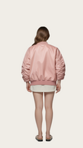 Person wearing a pink bomber jacket and white shorts on a gray background