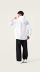 Person wearing a white hoodie and black pants on a plain background