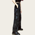Person wearing black floral pants and black shoes in a room with colorful walls.