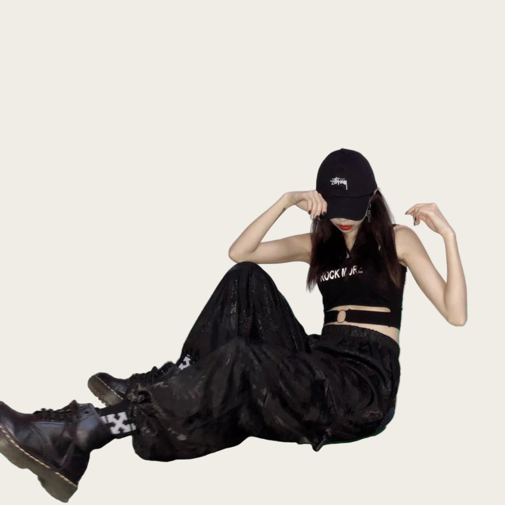 Person wearing a black outfit with text, sitting on a green floor against a pink and white striped wall.