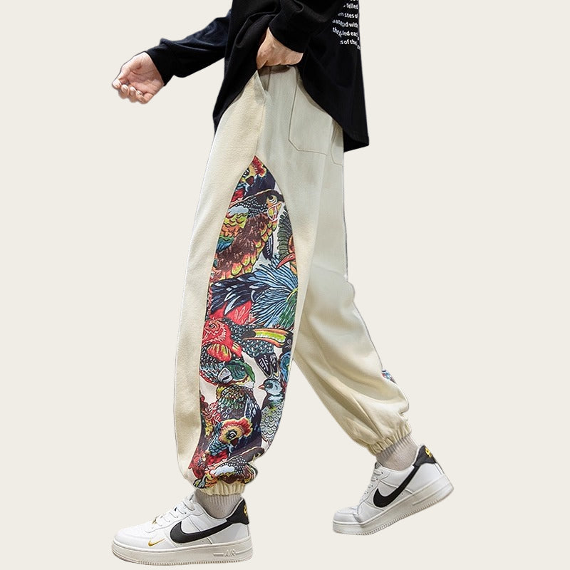 Person wearing beige sweatpants with a colorful floral pattern, white sneakers, and a black shirt in a room with a sewing machine and radio.