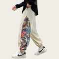 Person wearing beige sweatpants with a colorful floral pattern, white sneakers, and a black shirt in a room with a sewing machine and radio.
