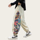 Person wearing beige sweatpants with a colorful floral pattern, white sneakers, and a black shirt in a room with a sewing machine and radio.
