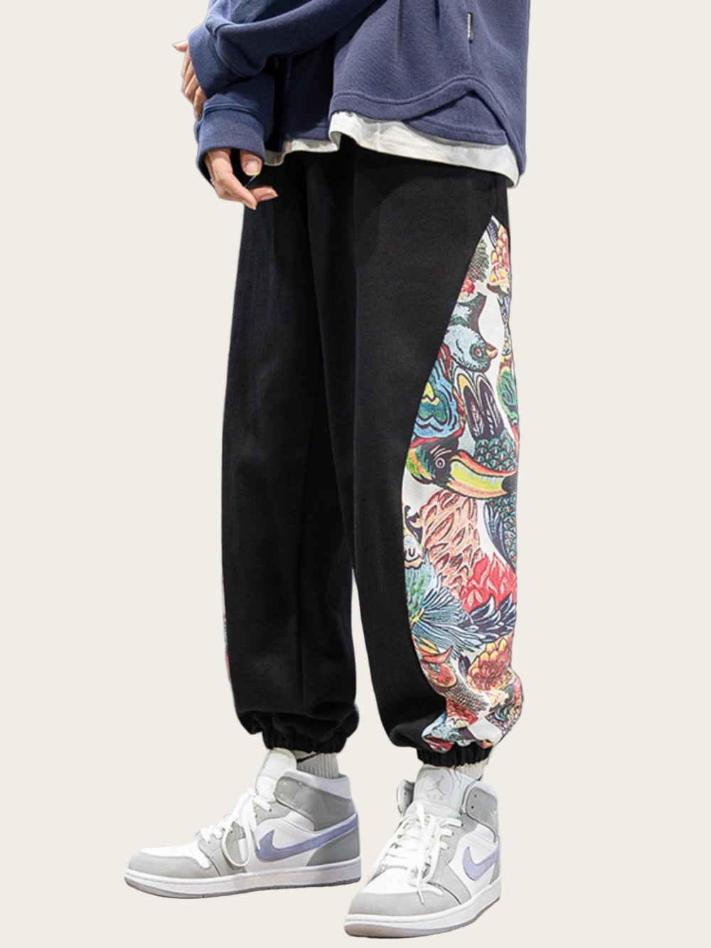 Person wearing black jogger pants with colorful side panels, white sneakers, and a blue jacket against a gray background.