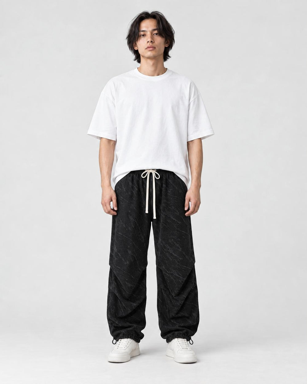 Model wearing the black acid-wash corduroy parachute pants with a white tee, front view