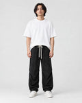 Model wearing the black acid-wash corduroy parachute pants with a white tee, front view