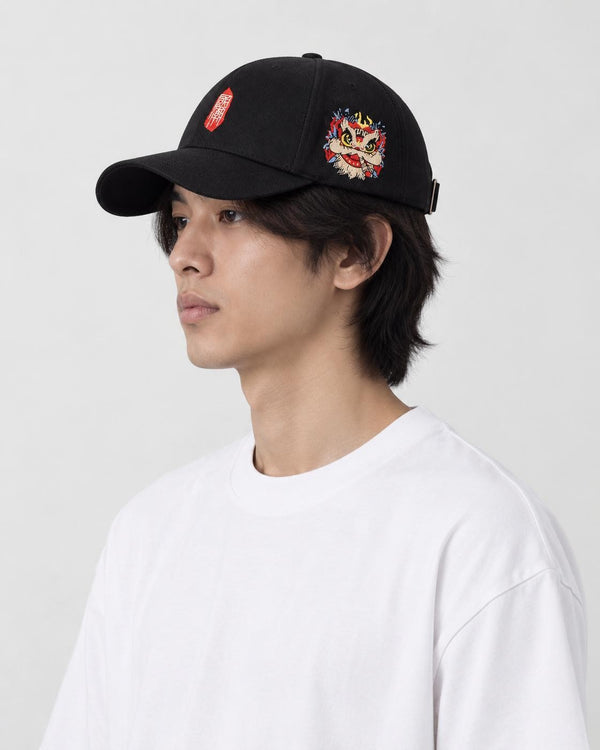 Man wearing the black baseball cap in profile, showing the embroidered lion-dance head on the side