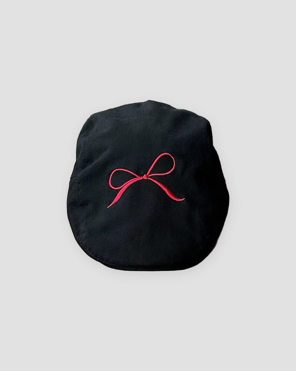 Black flat cap with a fine red bow embroidered on the crown