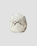 Cream flat cap with a fine dark brown bow embroidered on the crown