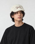 Model wearing the cream bow embroidered flat cap with a black tee, three-quarter view