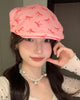 Woman wearing a pink flat cap with a scattered red bow print, one hand raised to her cheek, front view