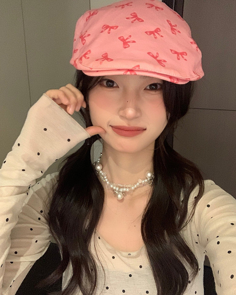 Front view of the pink bow print flat cap worn low over the forehead with a pearl necklace