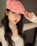 Woman holding the short peak of the pink bow print flat cap with one hand, three-quarter view