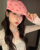 Woman holding the short peak of the pink bow print flat cap with one hand, three-quarter view