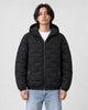 Model wearing the black quilted padded jacket zipped up over a white tee and light-wash jeans