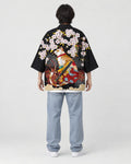 Full-length back view of a man in the black haori with a calico cat and a katana under pink blossoms, white tee and jeans
