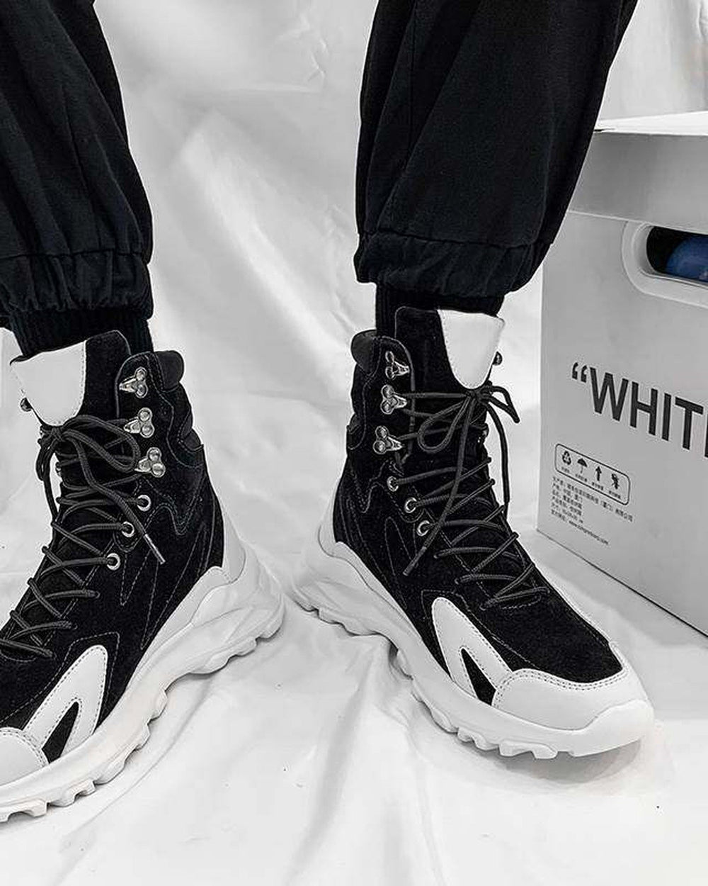 Black high-top sneakers worn with black cuffed pants, seen from the front