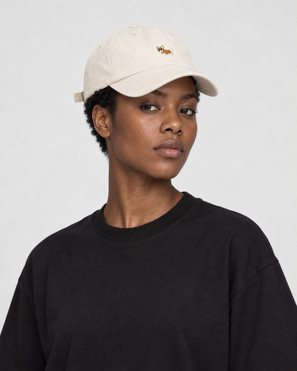 Woman wearing the cream corgi baseball cap with a black tee, three-quarter view