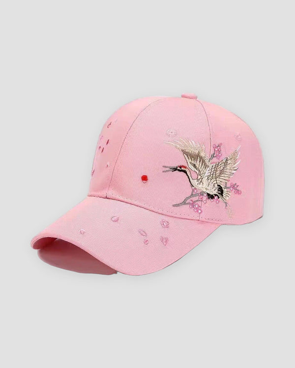 Pink baseball cap with a crane in flight embroidered over plum blossoms on the side of the crown