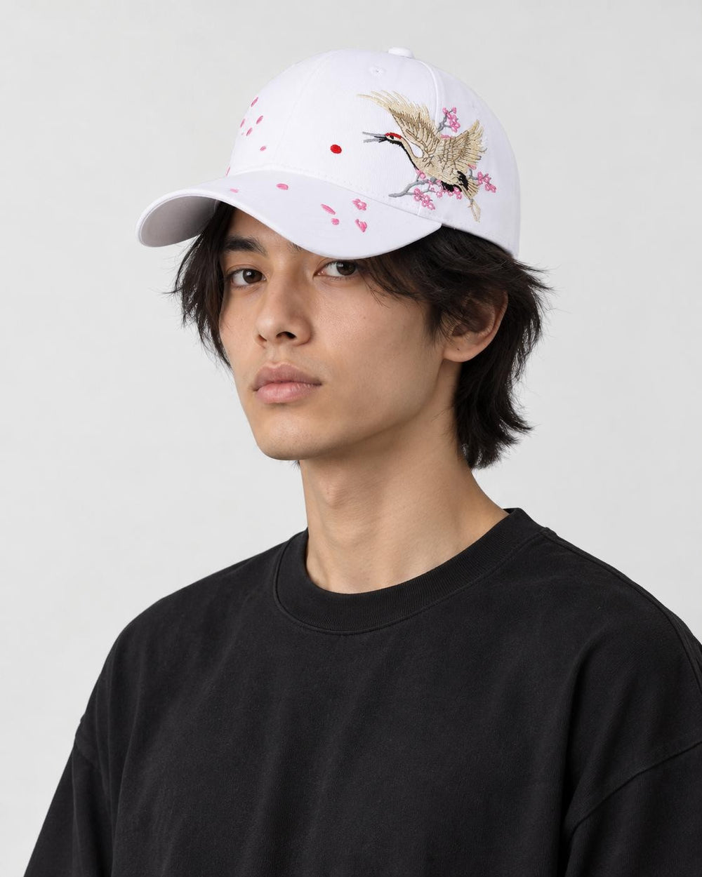Model wearing the white crane embroidered baseball cap with a black tee, three-quarter view