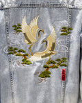 Close-up of the crane's white and gold wings among green pine branches