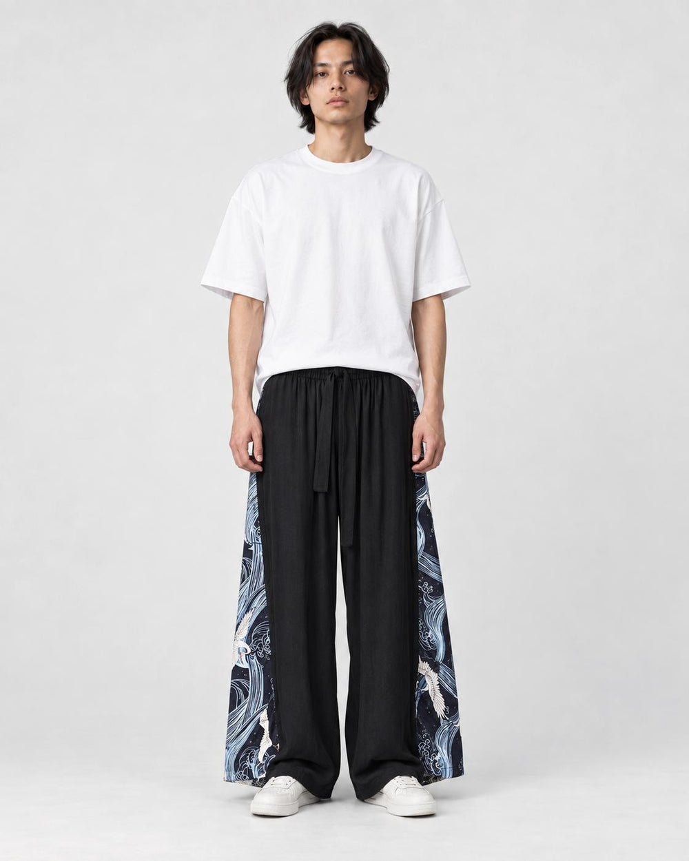 Model wearing the black wide-leg pants with dark navy crane and wave side panels and a white tee, front view