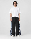 Model wearing the black wide-leg pants with dark navy crane and wave side panels and a white tee, front view
