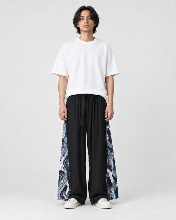 Model wearing the black wide-leg pants with dark navy crane and wave side panels and a white tee, front view