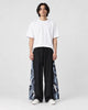 Model wearing the black wide-leg pants with dark navy crane and wave side panels and a white tee, front view